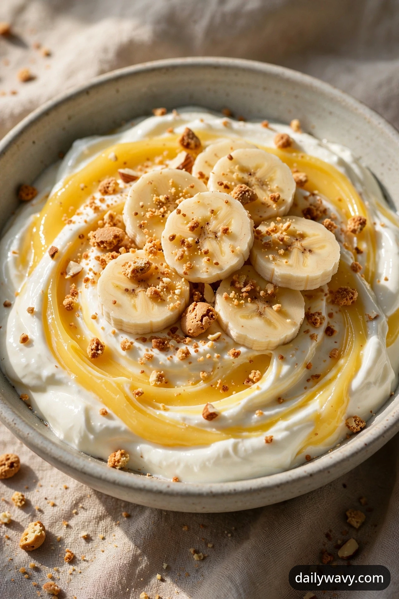 A banana yogurt bowl with bright yellow lemon curd ribbons swirled through the yogurt, with banana coins and crushed amaretti crumbs on top.
