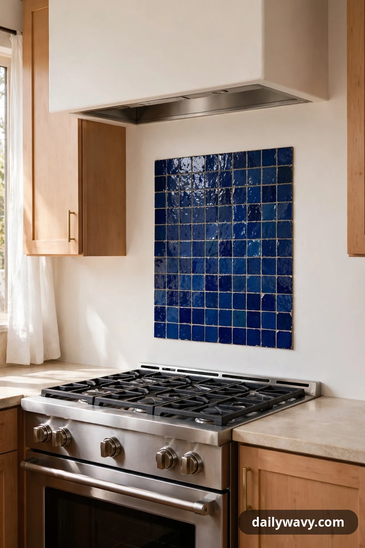 A square panel of glossy cobalt blue handmade-look tiles covers the wall behind a gas cooktop, surrounded by plain warm white plaster and light wood cabinets.