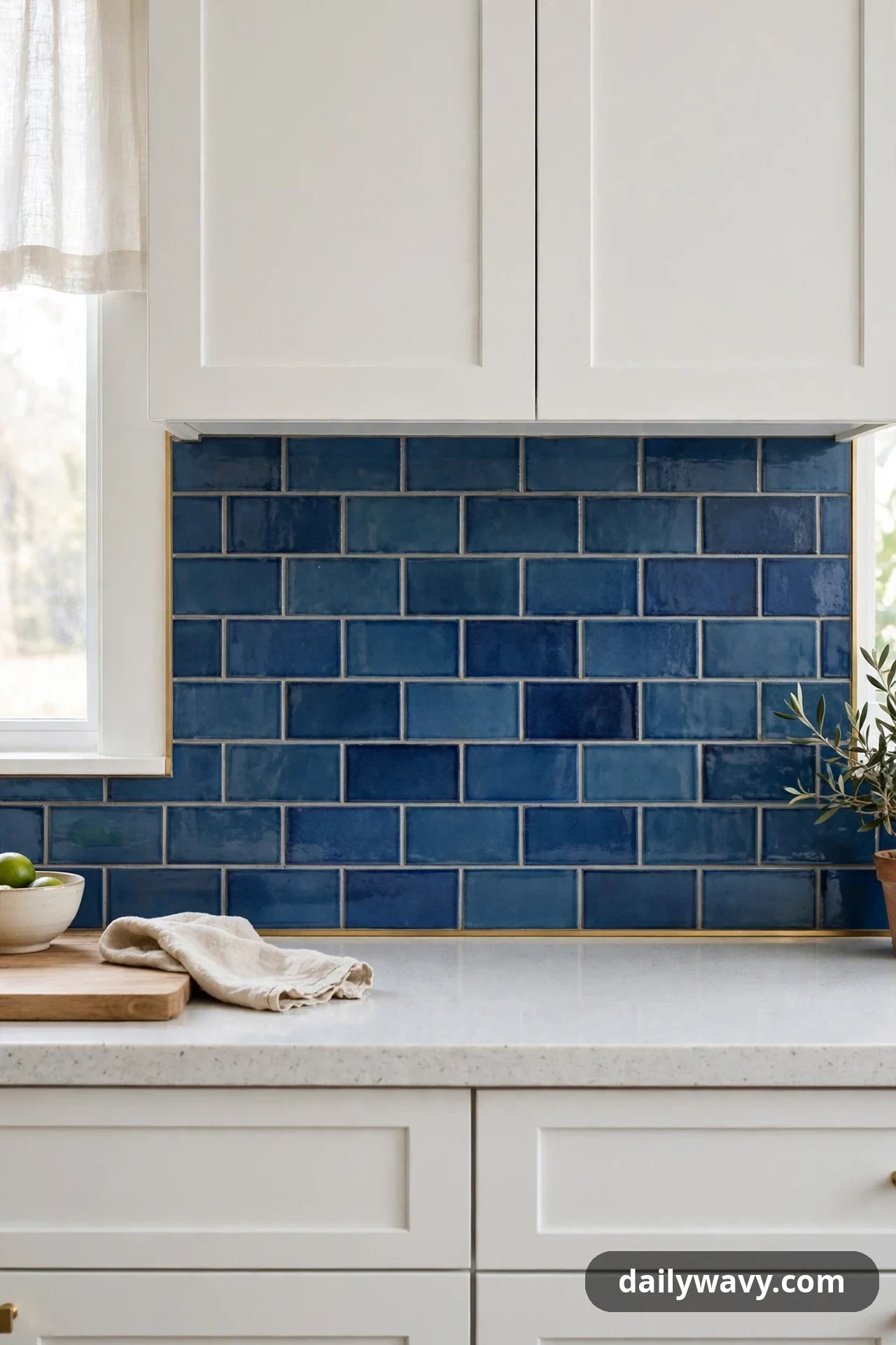 Glossy deep blue subway tiles meet a white countertop along a thin brass edge trim, below white shaker cabinets.