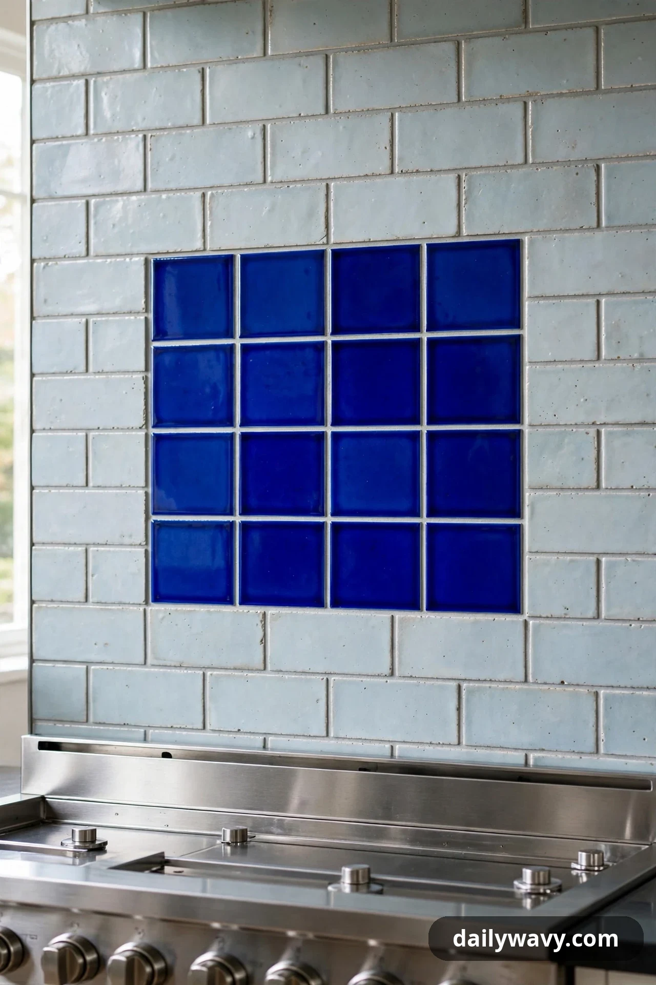 A panel of saturated cobalt blue square tiles is set into a wall of pale gray-blue subway tile above a stainless steel range.