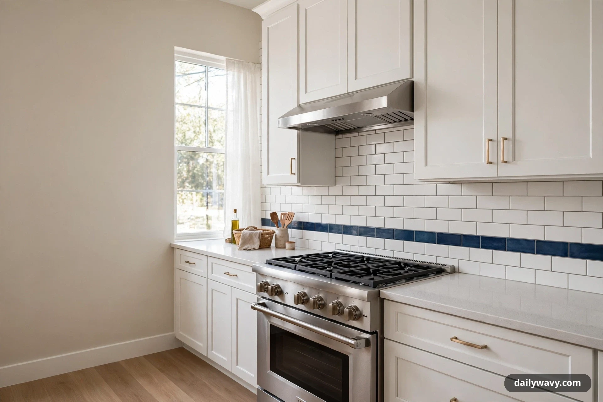 A wide view of a white shaker kitchen shows a white subway tile backsplash crossed by a single horizontal stripe of deep blue tile above a stainless steel gas range.