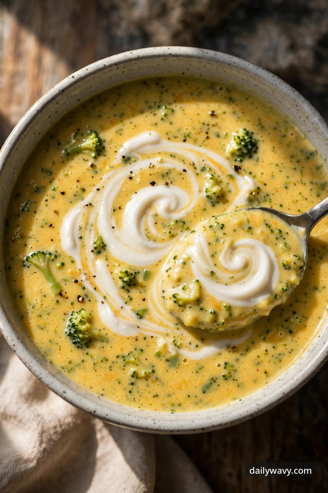 Broccoli cheddar soup with coconut cream in a ceramic bowl with a spoon showing the silky swirl