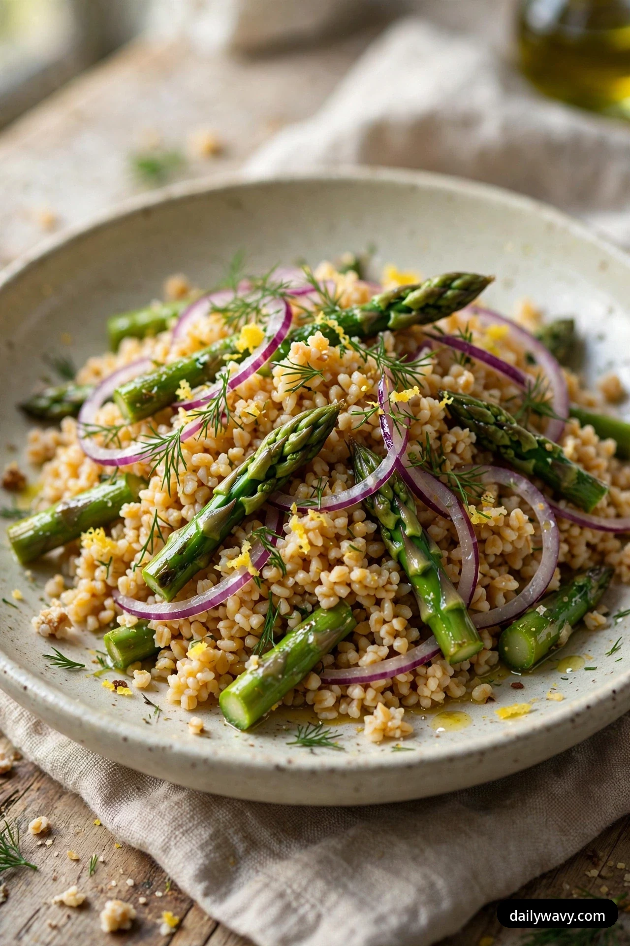 A close three-quarter view of bulgur salad with asparagus pieces, thin red onion rings, fresh dill fronds and lemon zest in a shallow bowl.