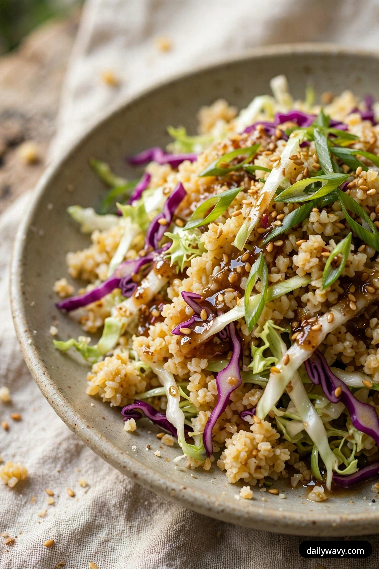 A close view of fine bulgur salad tossed with shredded green and red cabbage and a glossy sesame dressing is topped with toasted sesame seeds and sliced scallions.