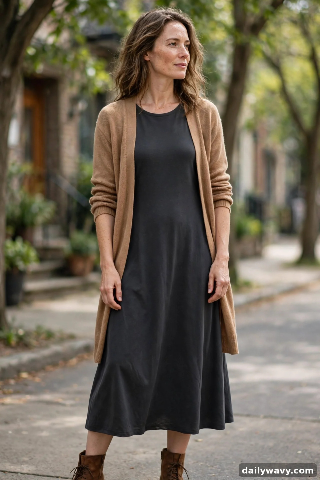 Woman in camel cardigan over dark grey midi dress with brown ankle boots