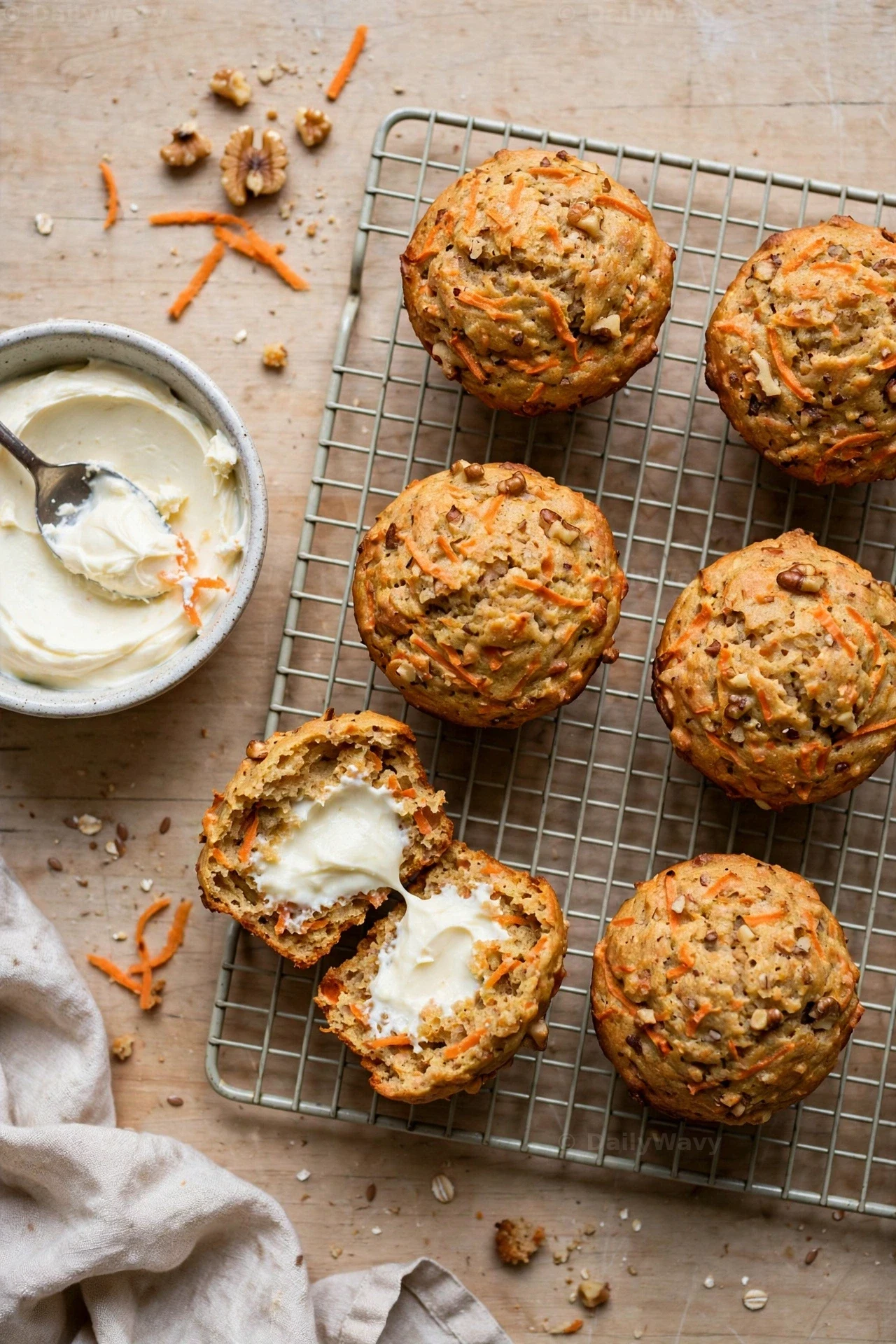 Cream-cheese-center carrot muffins cool on a wire rack beside a bowl of cream cheese filling, and one muffin is pulled apart to show the white center inside.