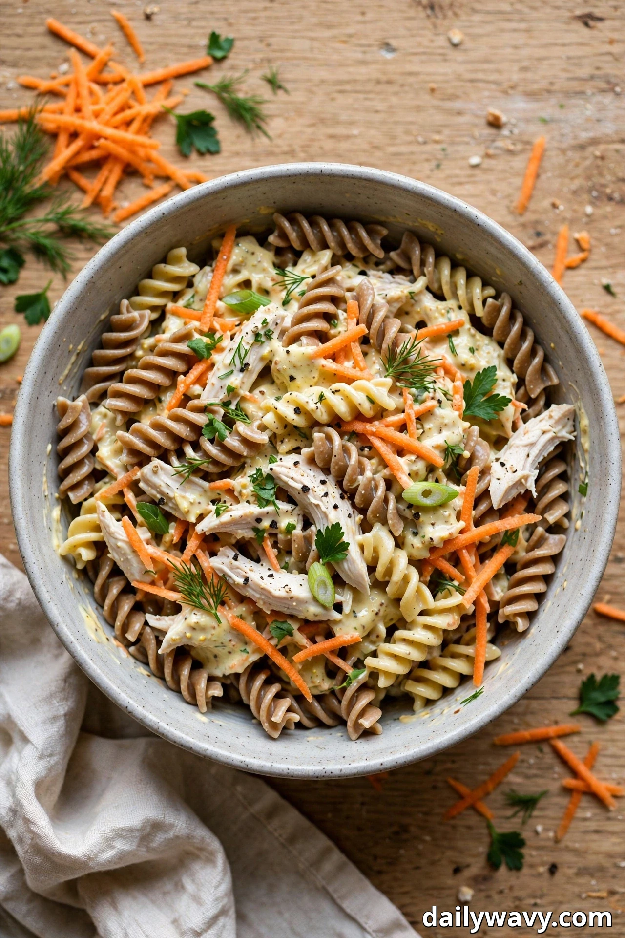 A speckled bowl holds whole-wheat fusilli pasta salad tossed with shredded chicken, shredded carrots and sliced scallions in a creamy honey-mustard yogurt dressing.