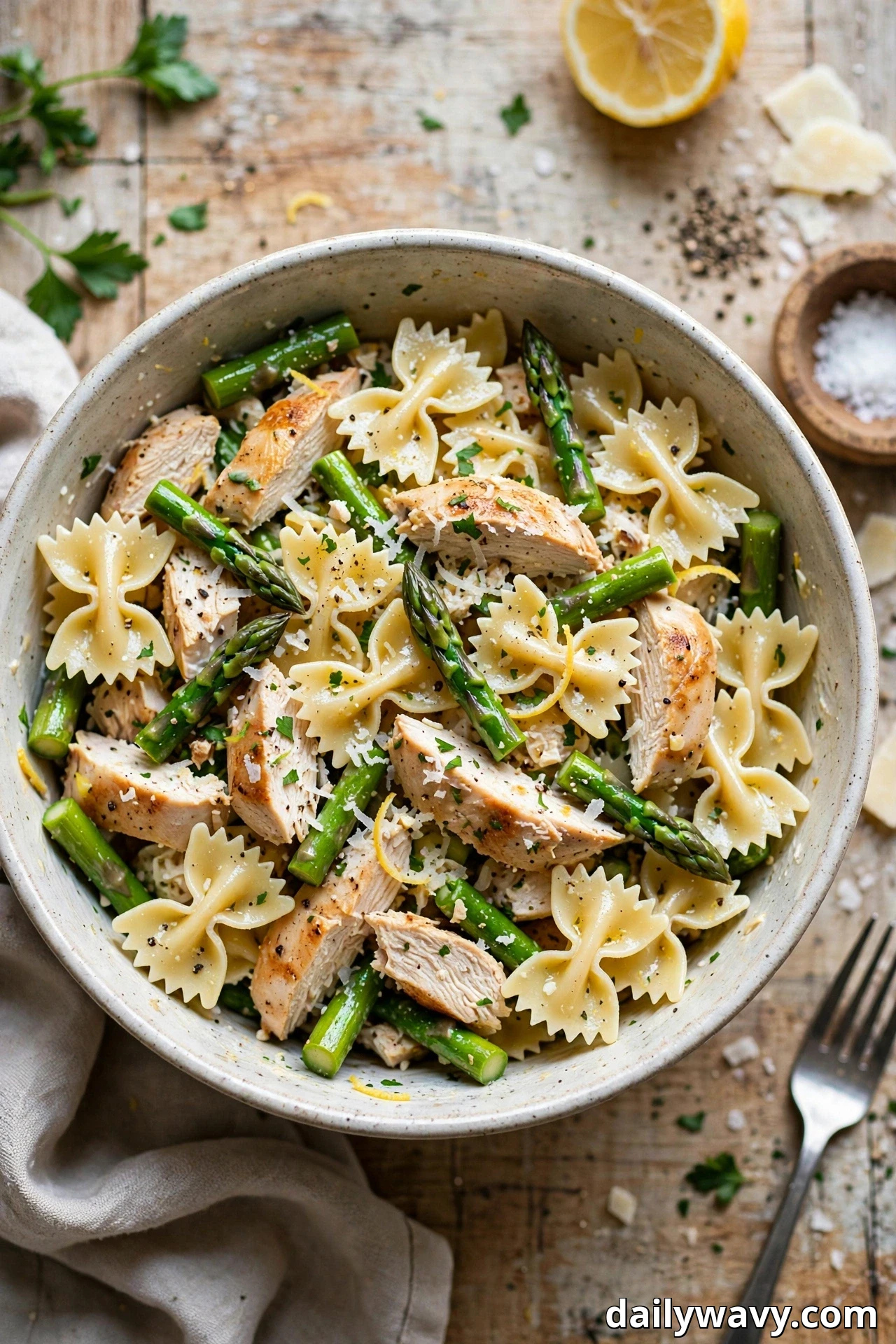 A speckled bowl holds farfalle pasta salad tossed with asparagus spears, sliced chicken and grated Parmesan.