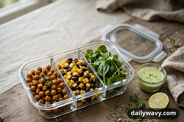 Roasted chickpeas, a corn and black bean mix and leafy greens fill the three compartments of a glass meal-prep container, with a small cup of green herb dressing and a halved lime beside it