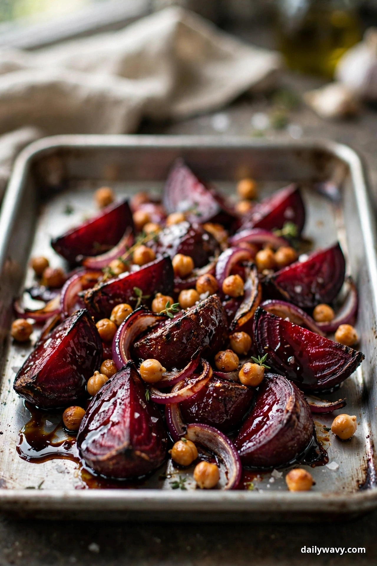 Glossy roasted beet wedges, red onion slices and chickpeas coated in a dark balsamic glaze fill a sheet pan in close view