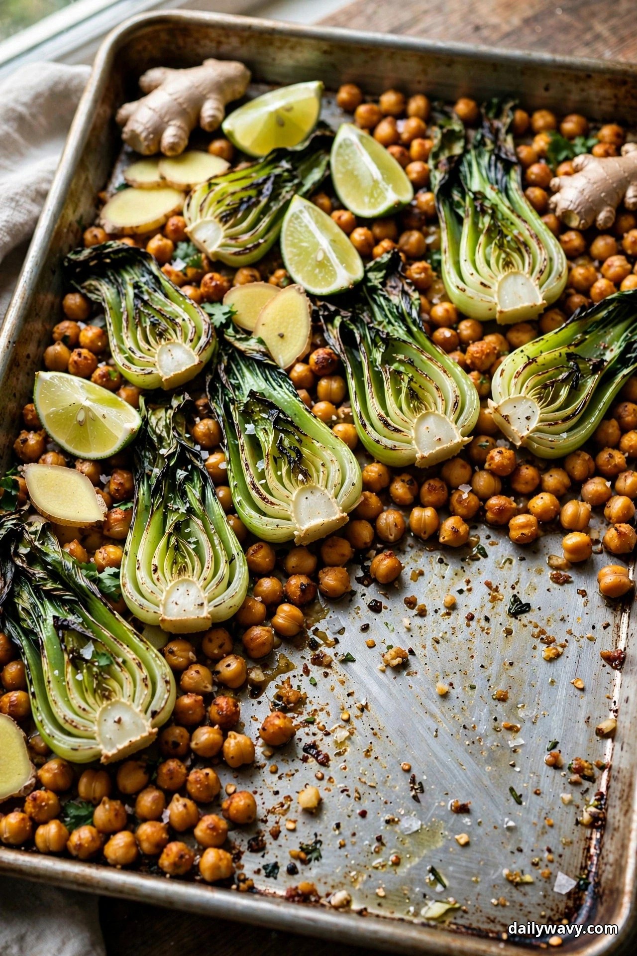 Halved baby bok choy with charred leaves, roasted chickpeas and lime wedges fill a sheet pan with one serving already removed