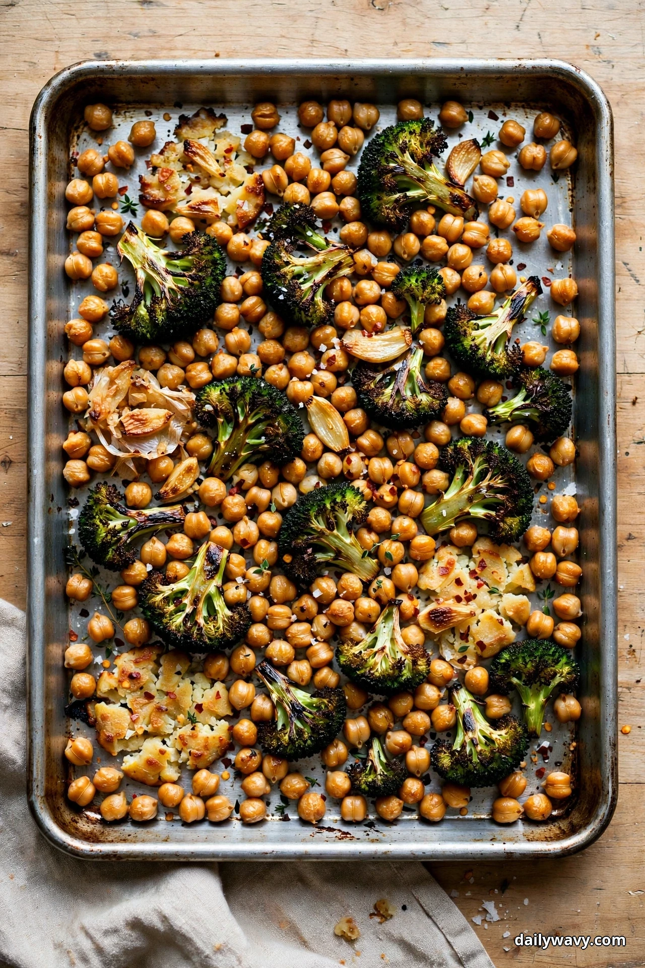 Seen from above, charred broccoli florets, roasted garlic cloves and chickpeas with red pepper flakes cover a metal sheet pan