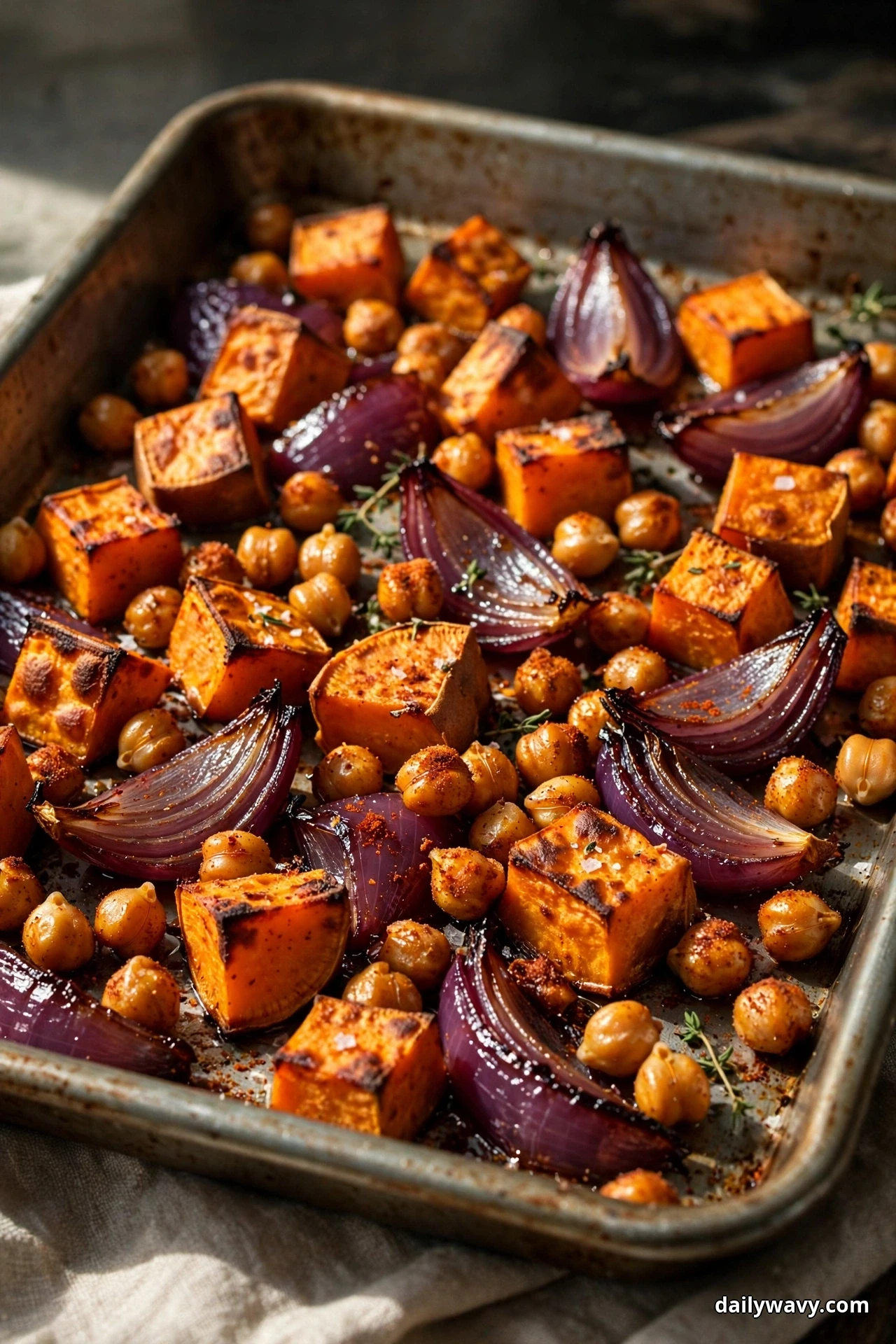 Caramelized sweet potato cubes, red onion wedges and spice-dusted chickpeas fill a metal sheet pan in close view