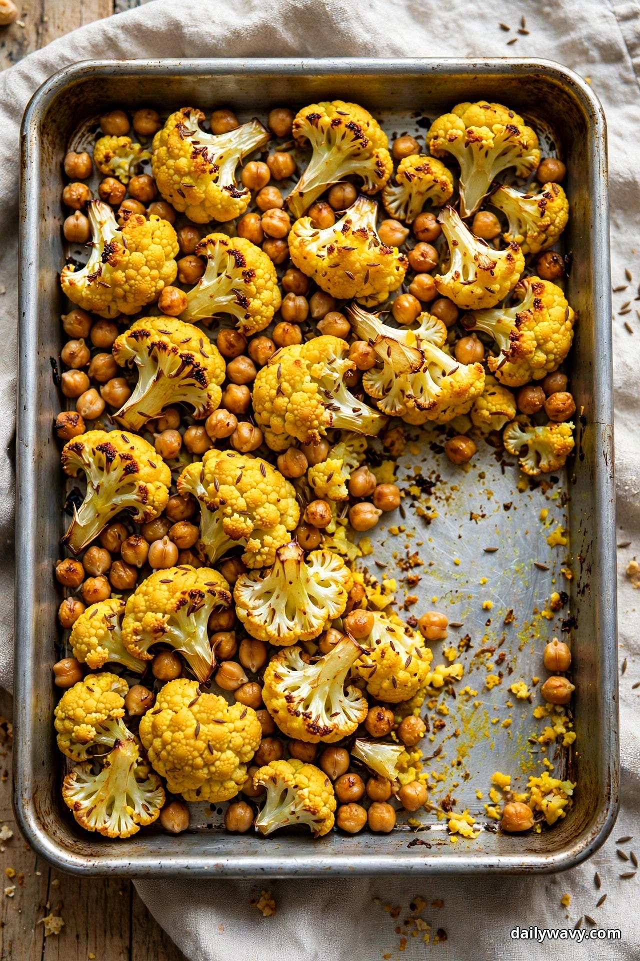 Turmeric-golden cauliflower florets and chickpeas fill a sheet pan with one serving removed, seen from above