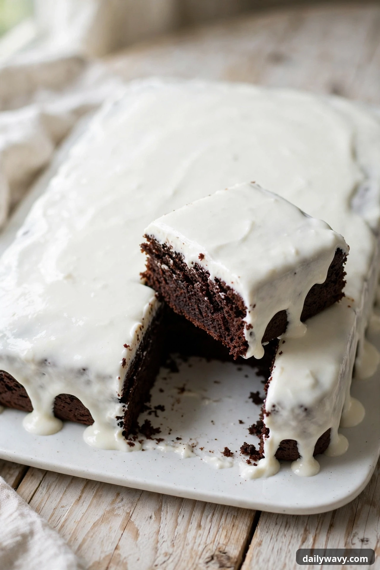 Chocolate sheet cake with white yogurt glaze and a cut square showing the crumb