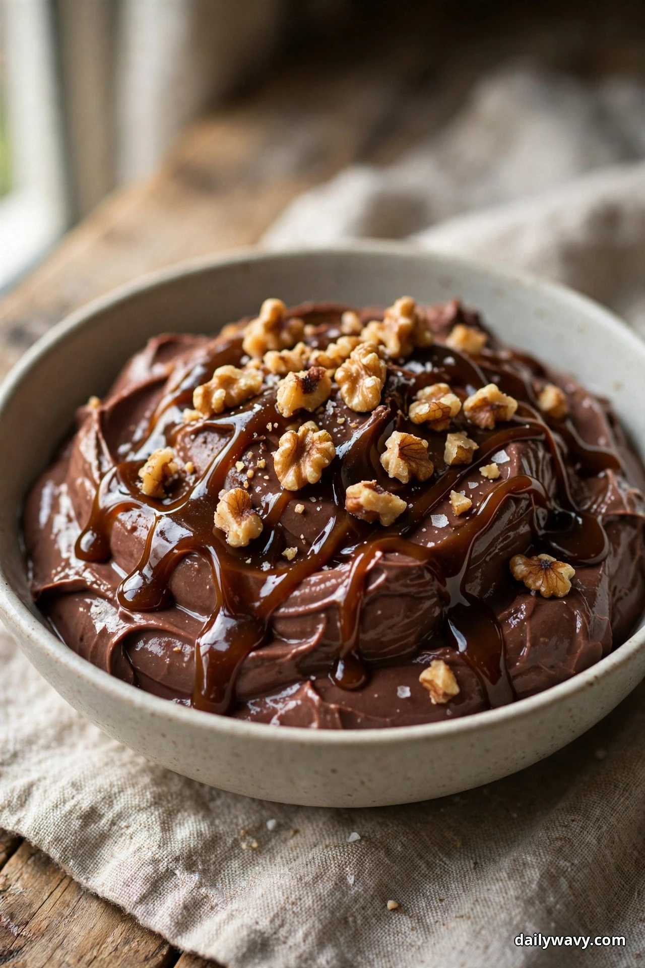 A bowl of chocolate yogurt is drizzled with glossy date caramel and topped with toasted walnut pieces and flakes of sea salt