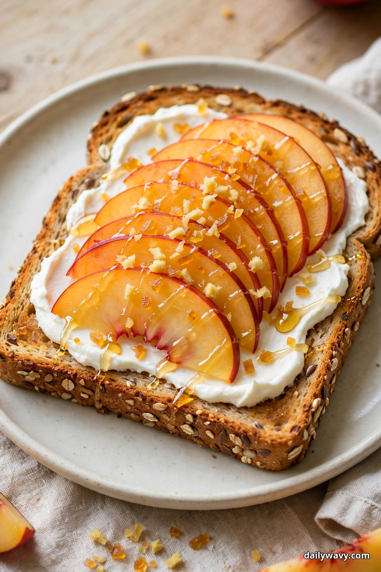 A slice of multigrain toast spread with cream cheese is topped with fanned nectarine slices, minced crystallized ginger and a honey drizzle