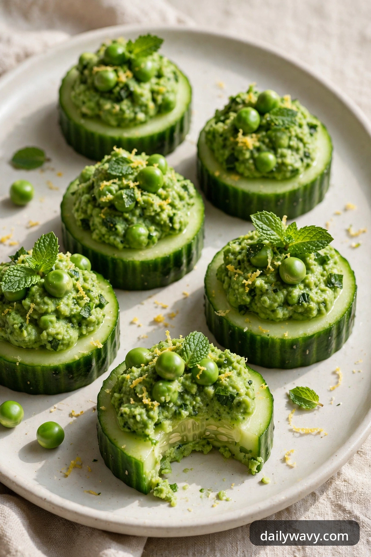 Cucumber rounds with vibrant green pea mint puree, whole peas, a small mint leaf and lemon zest