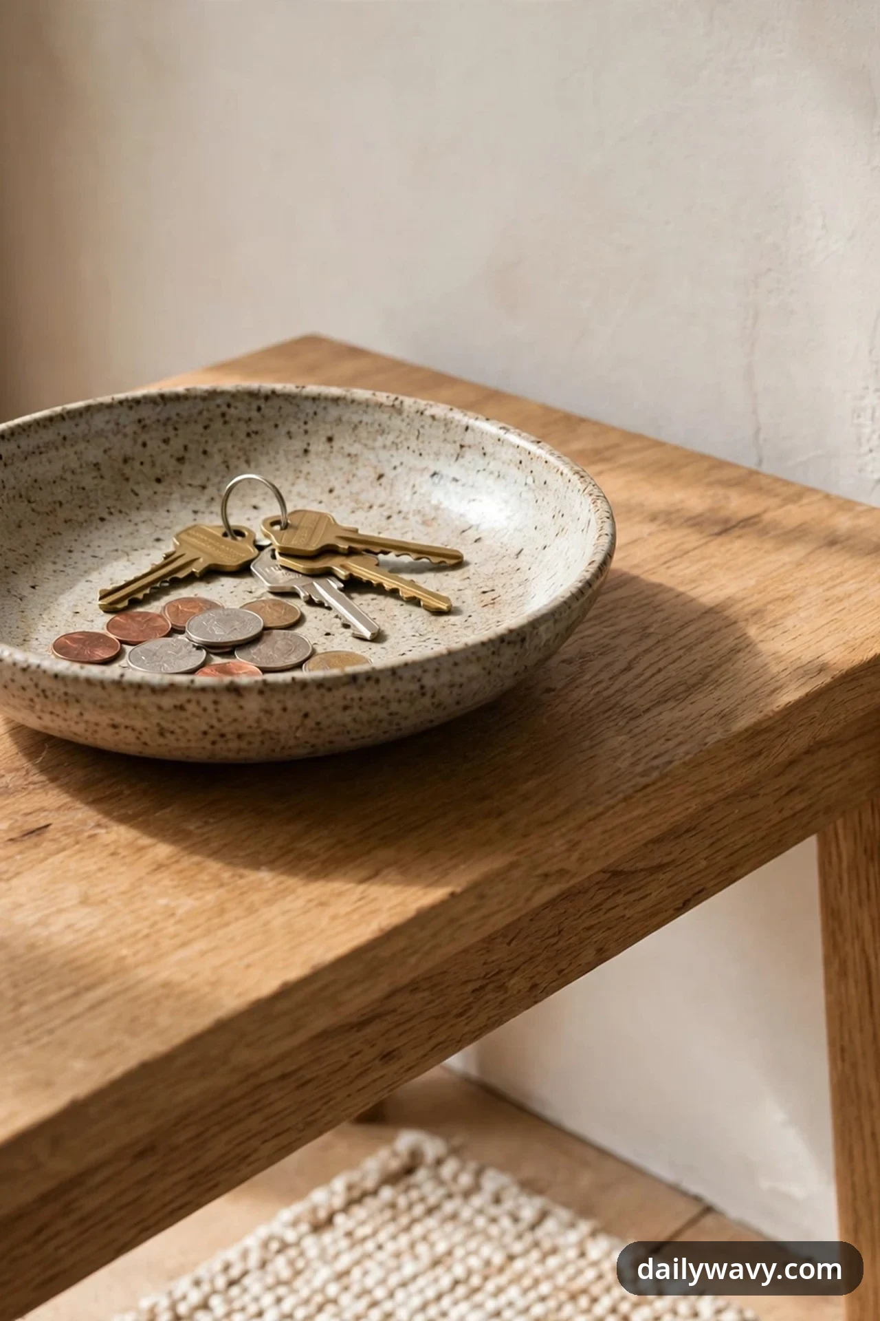 A shallow speckled ceramic bowl holding a set of keys and loose coins sits on a wooden console table.