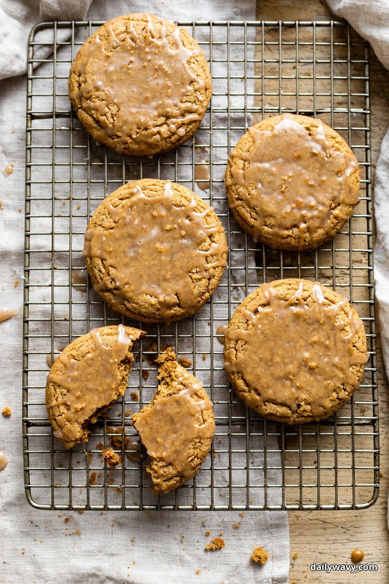 Round ginger cookies coated in a shiny maple glaze cool on a wire rack, with one cookie broken in two at the front of the rack