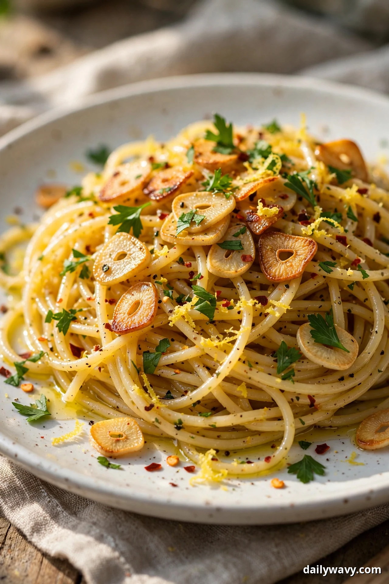 A plate of lemon garlic spaghetti holds crisped sliced garlic, chopped parsley, lemon zest, and red pepper flakes