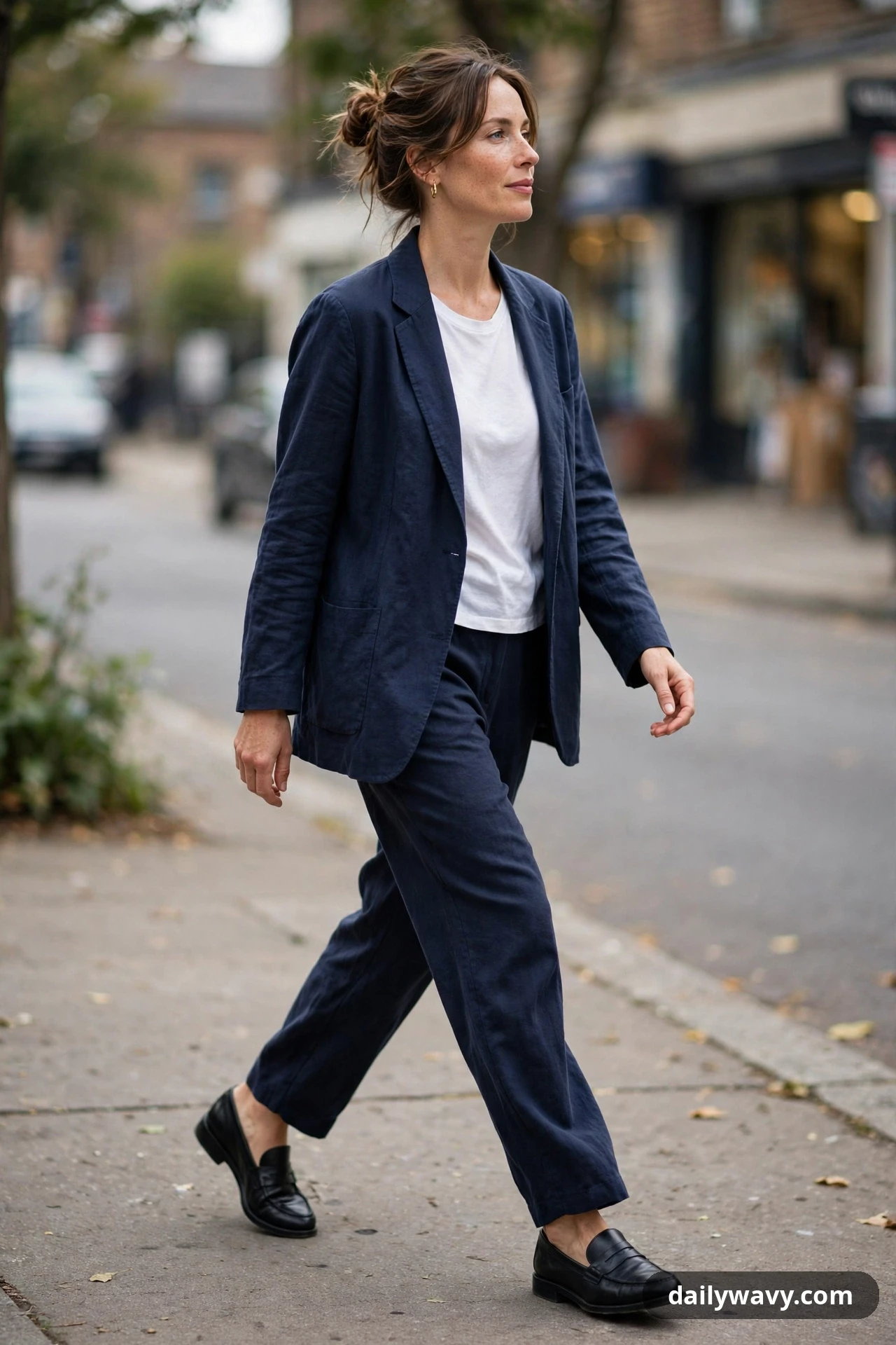 A woman walks in a relaxed navy suit with a plain white tee underneath and black loafers.