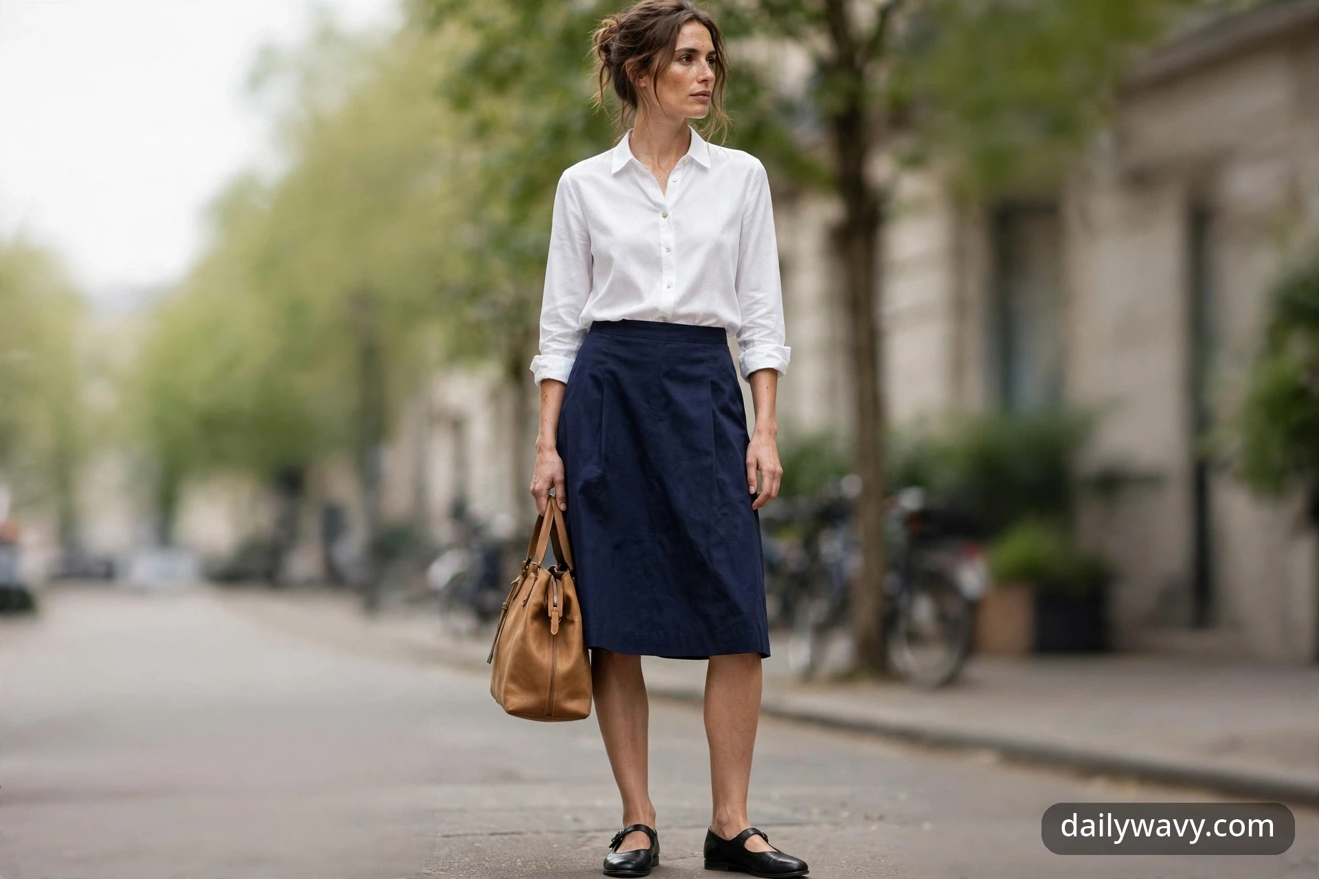 Adult model wearing a navy A-line skirt, white cotton blouse and black flat Mary Jane shoes, full-body outdoor view.