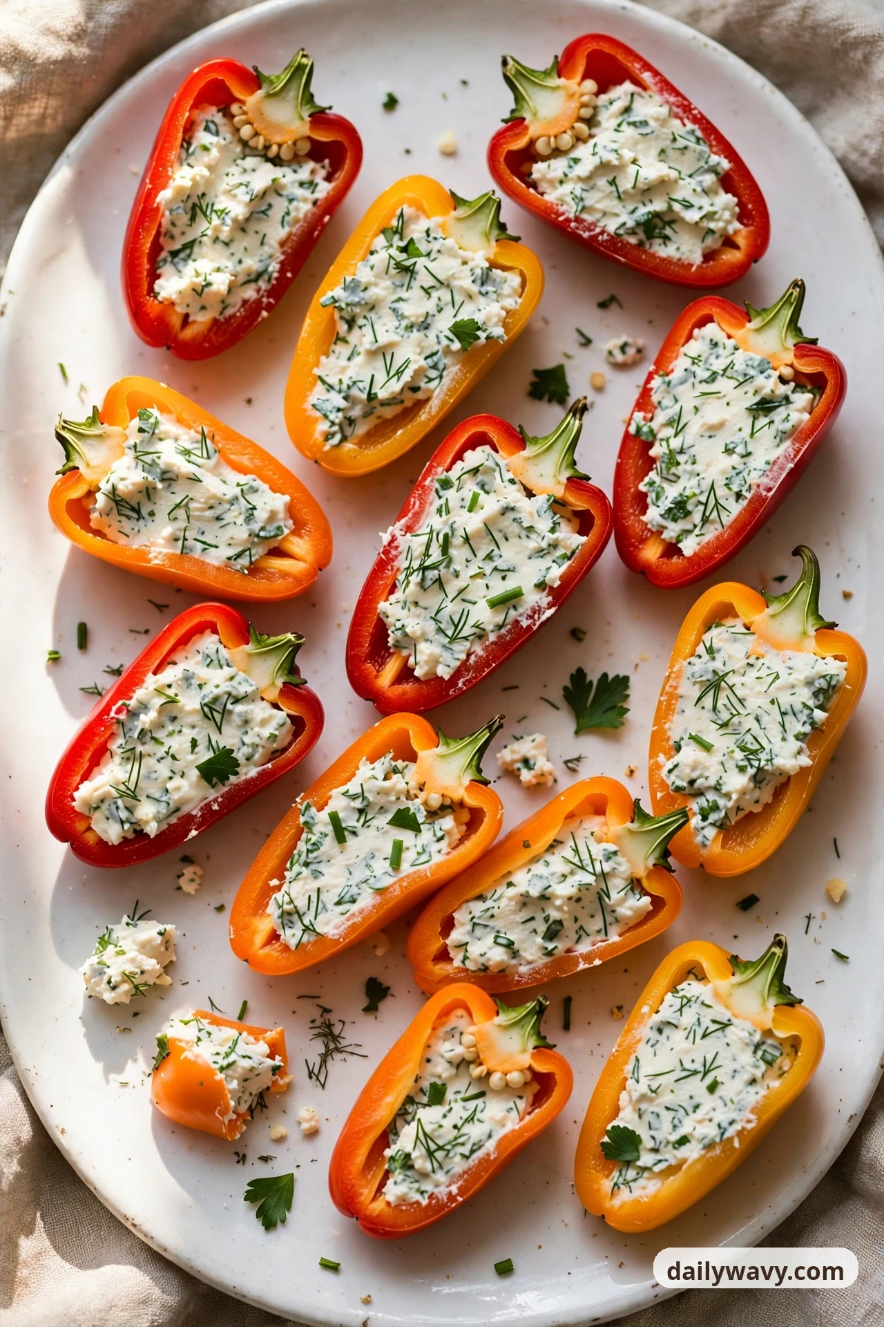 Mini sweet pepper halves on a white platter are filled with herbed cream cheese flecked with chopped dill, chives and parsley.
