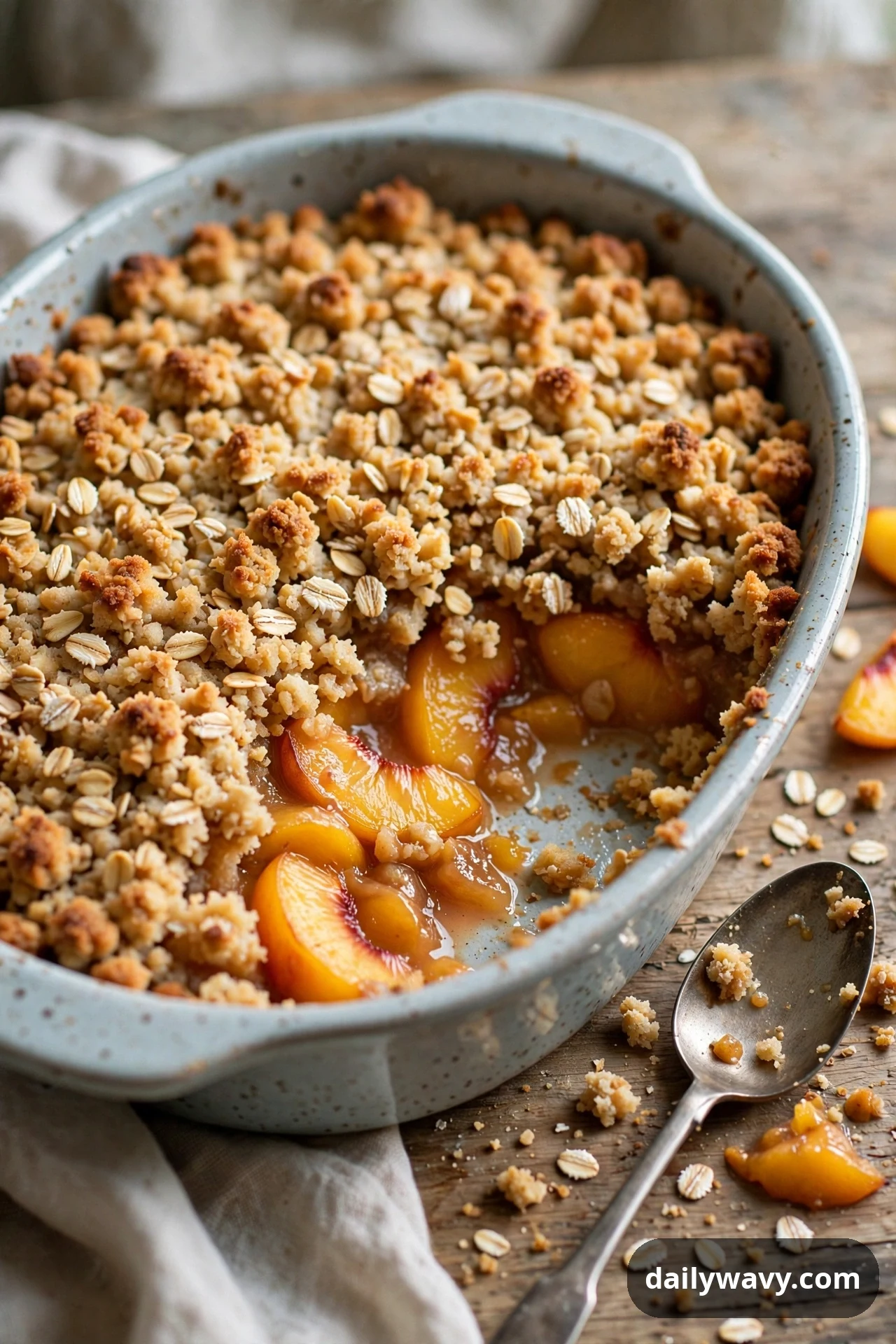 A baking dish of peach oat crisp shows a golden crumb topping with one serving spooned out, revealing the baked peach slices underneath.