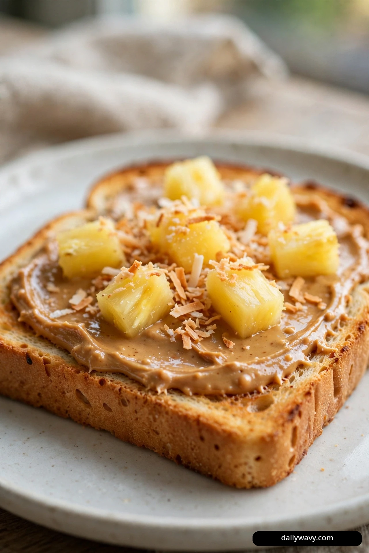 A close view shows a slice of toast spread with peanut butter and topped with pineapple chunks and toasted coconut flakes.
