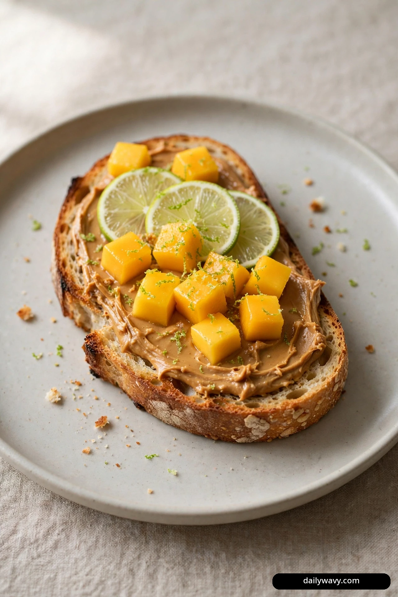 A top-down view shows a slice of toast spread with peanut butter and topped with diced mango and thin lime wheels.