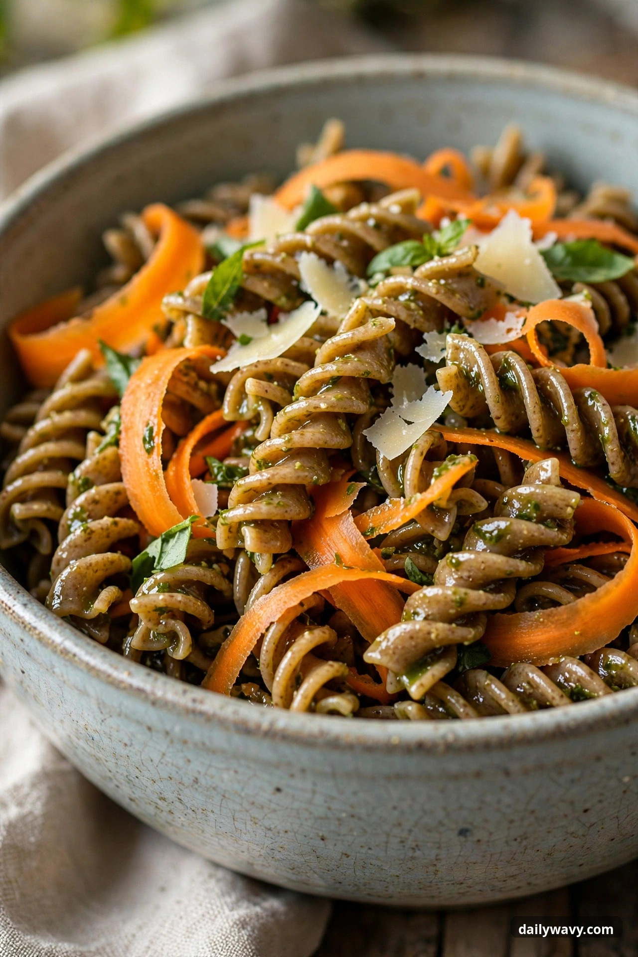 Pesto pasta salad with whole-wheat twists and carrots in a mixing bowl