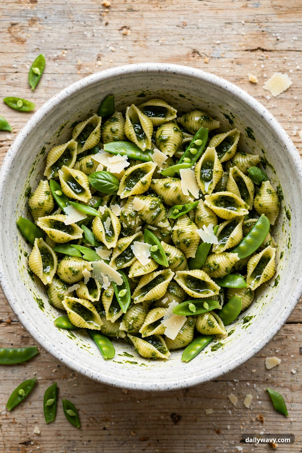 Pesto pasta salad with small shells and snap peas in a mixing bowl