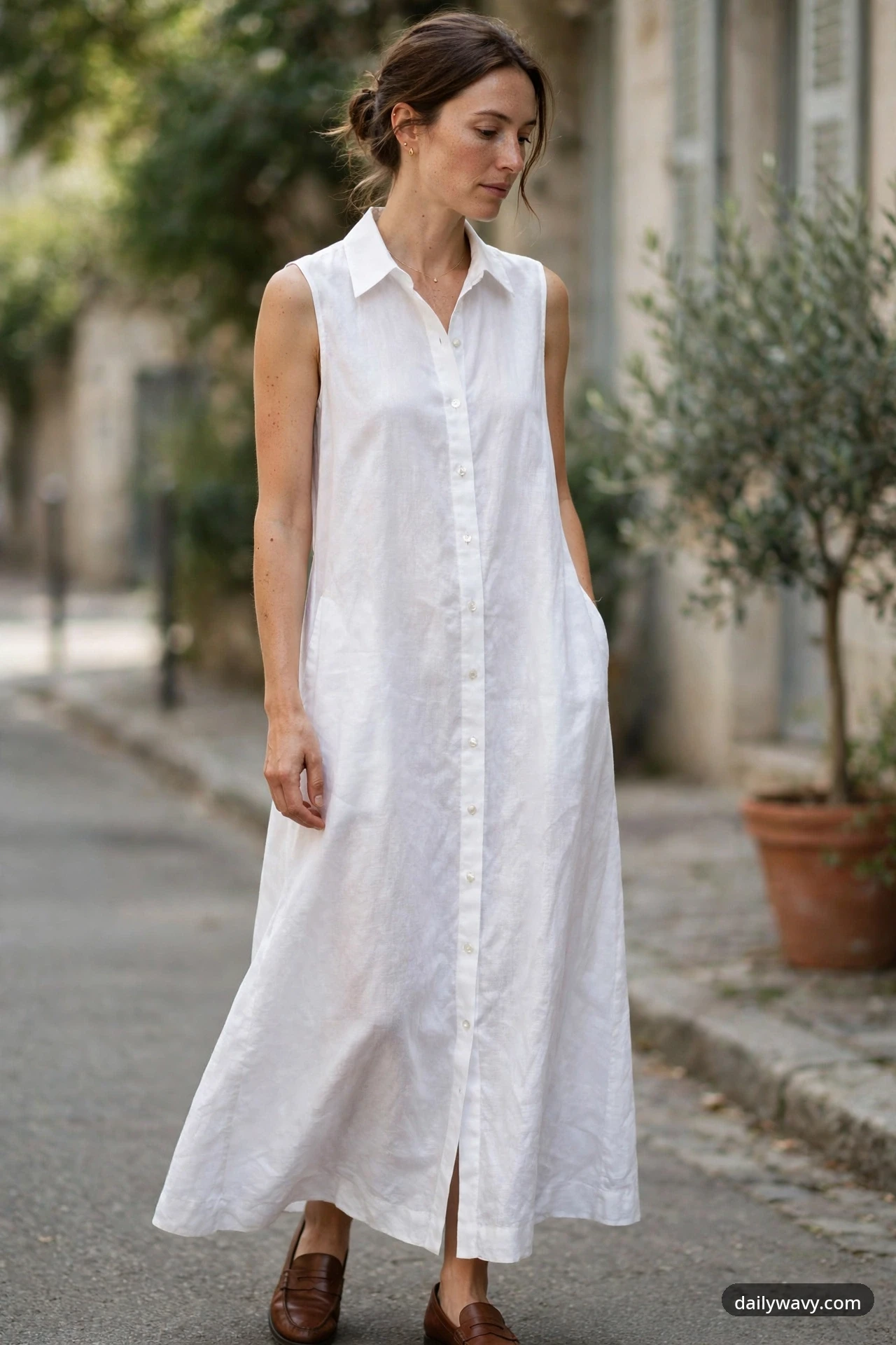 A petite woman stands on a sidewalk wearing a white sleeveless collared button-front shirt-dress maxi with delicate gold jewelry and brown loafers.