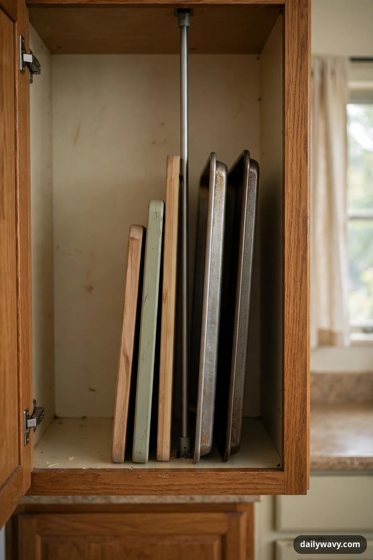 A vertical tension rod inside an open kitchen cabinet separates upright cutting boards from metal baking sheets