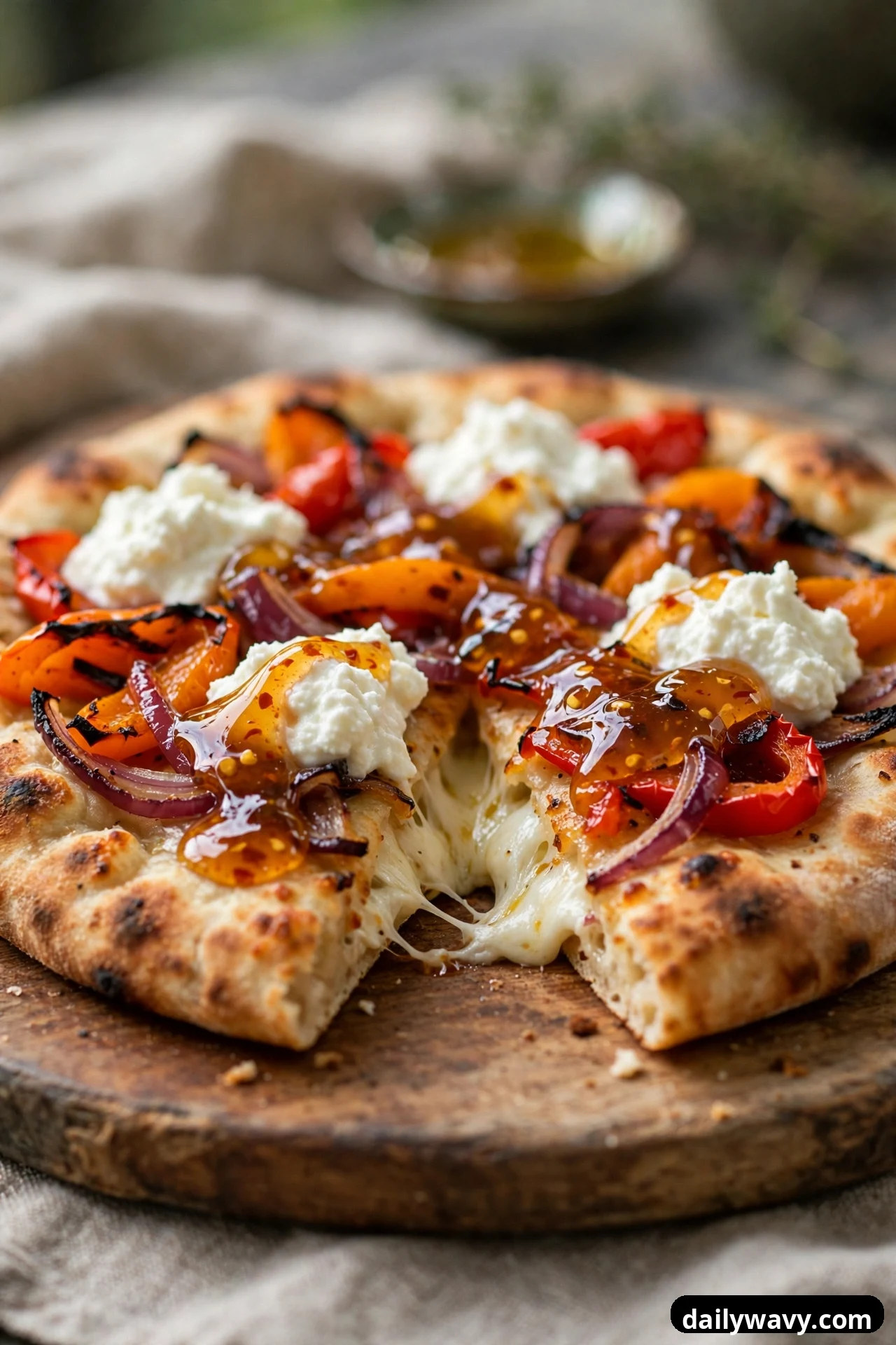 A flatbread topped with roasted bell pepper strips, red onion slices, and ricotta dollops is finished with a glossy chili honey drizzle, with one slice pulled away to show the melted cheese.