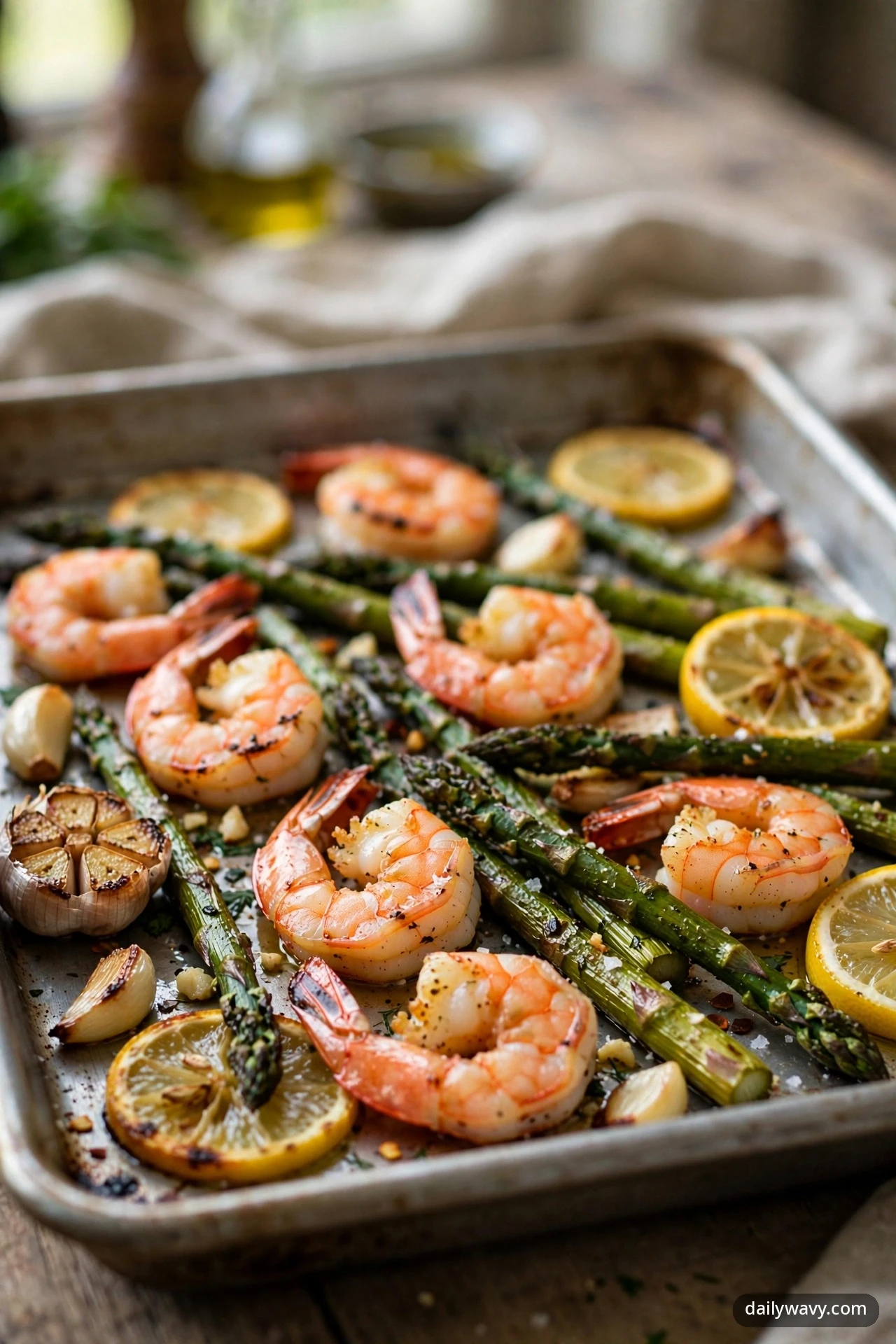 Roasted shrimp rest among charred asparagus spears, roasted lemon slices and whole garlic cloves, finished with red pepper flakes on a sheet pan.