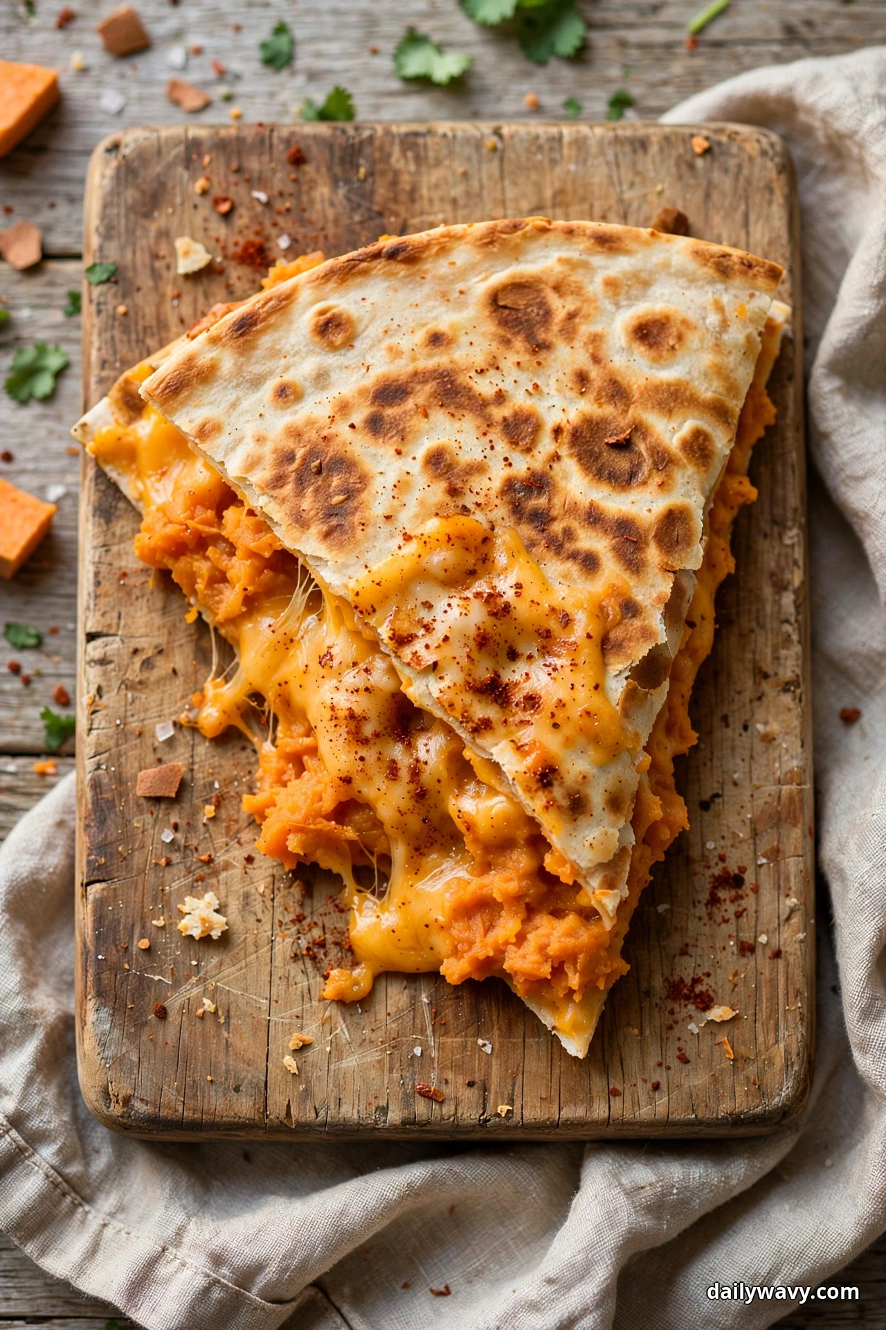 Two stacked wedges of sweet potato quesadilla on a wooden board show orange mashed filling with melted cheddar and a dusting of smoked paprika