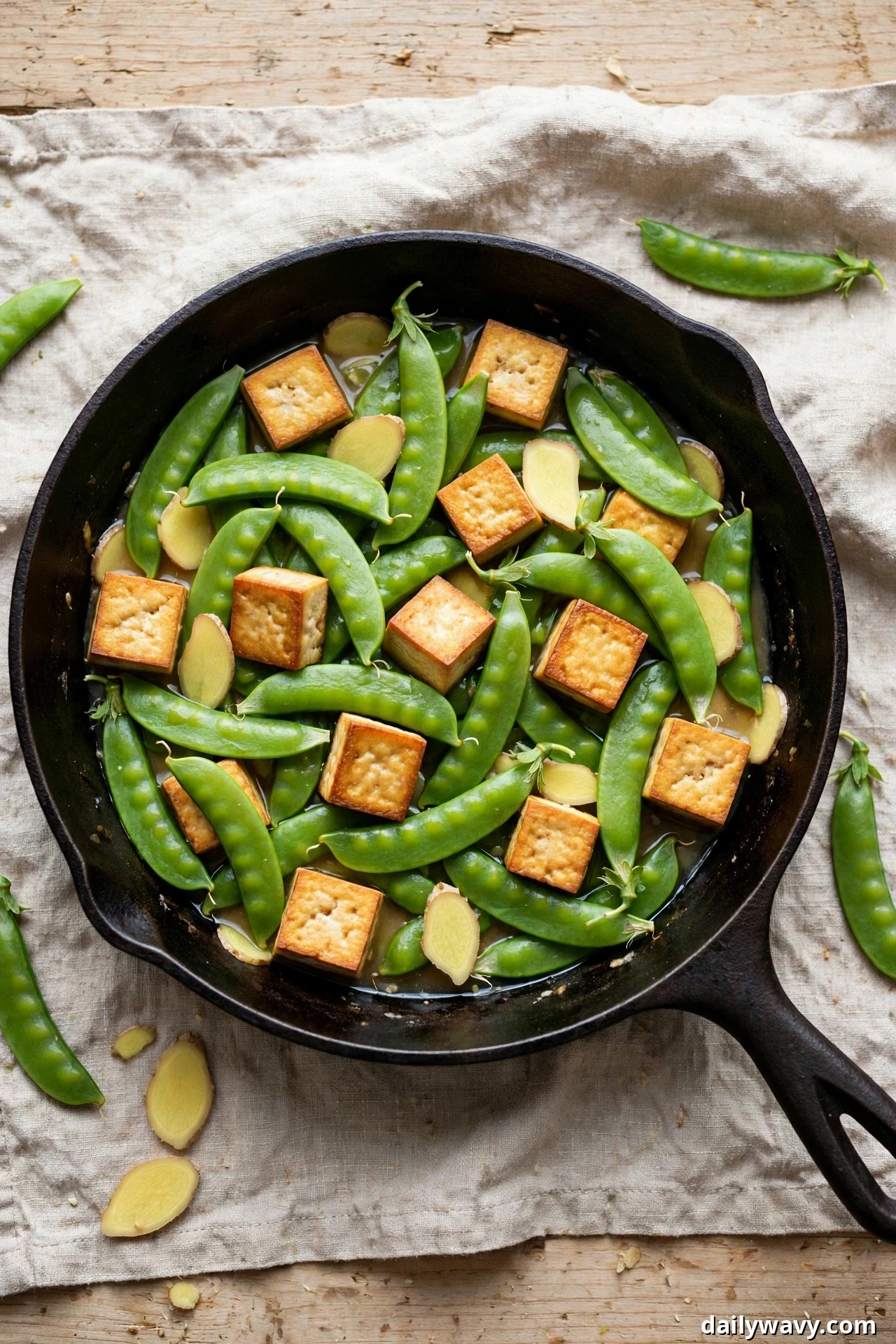 Golden tofu cubes, whole sugar snap peas, and thick slices of fresh ginger simmer in a light sauce in a cast-iron skillet.