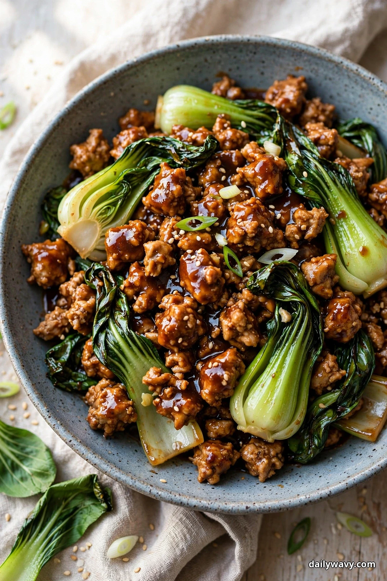 A speckled bowl of glossy hoisin-glazed ground turkey crumbles is packed with whole baby bok choy and rests on a linen cloth
