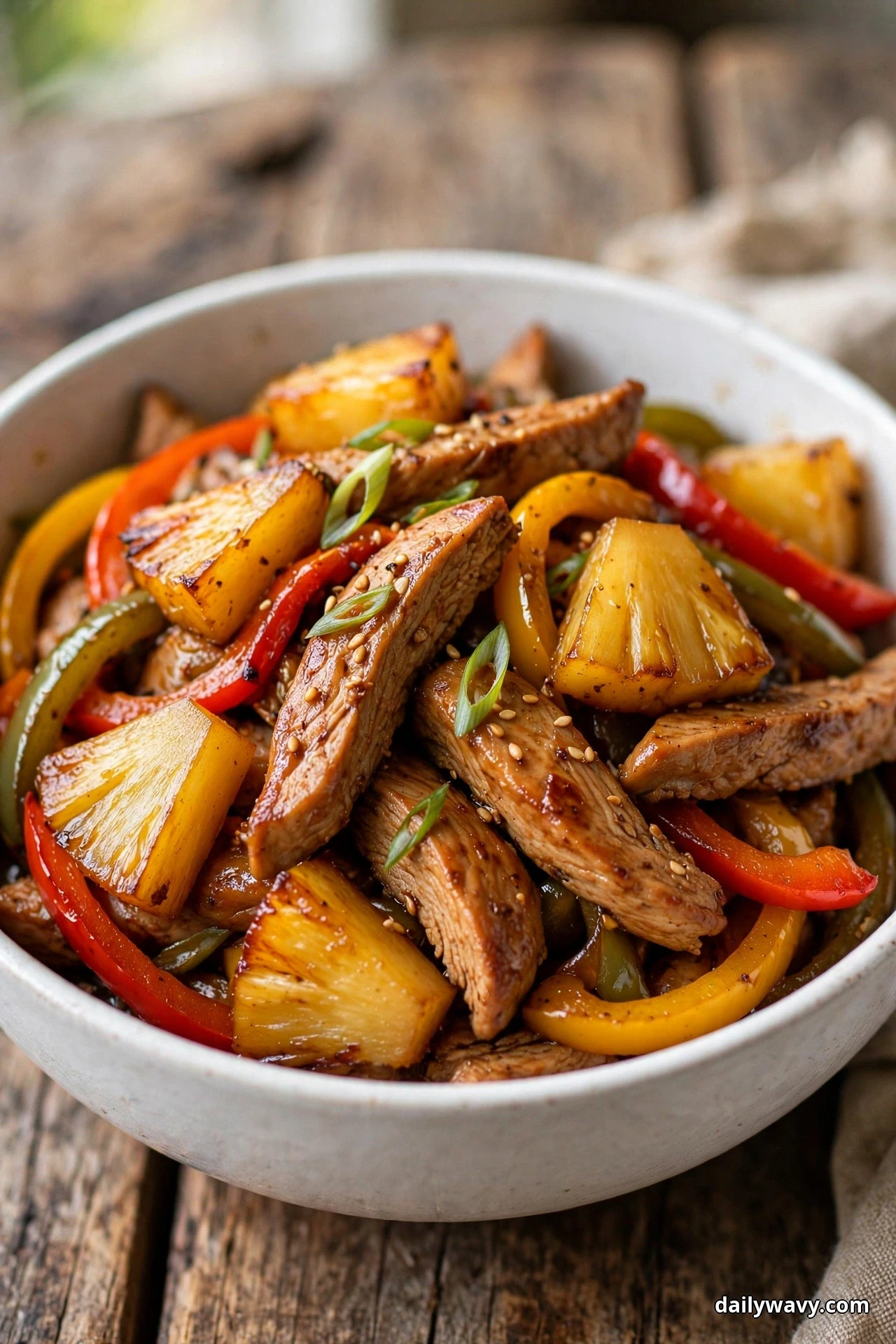 A white bowl of sliced glazed turkey strips is mixed with caramelized pineapple chunks, red, yellow and green bell pepper strips and sliced scallion greens