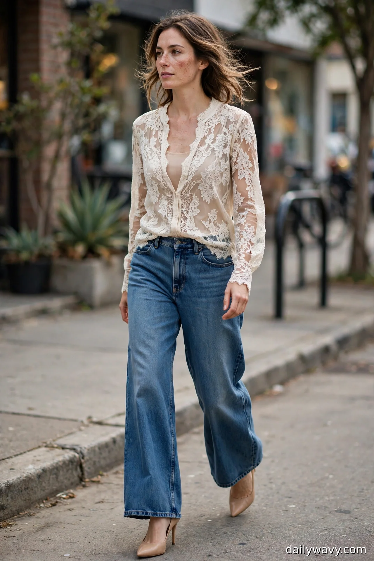 Woman in an ivory lace blouse with nude lining and nude pointed pumps with wide-leg jeans