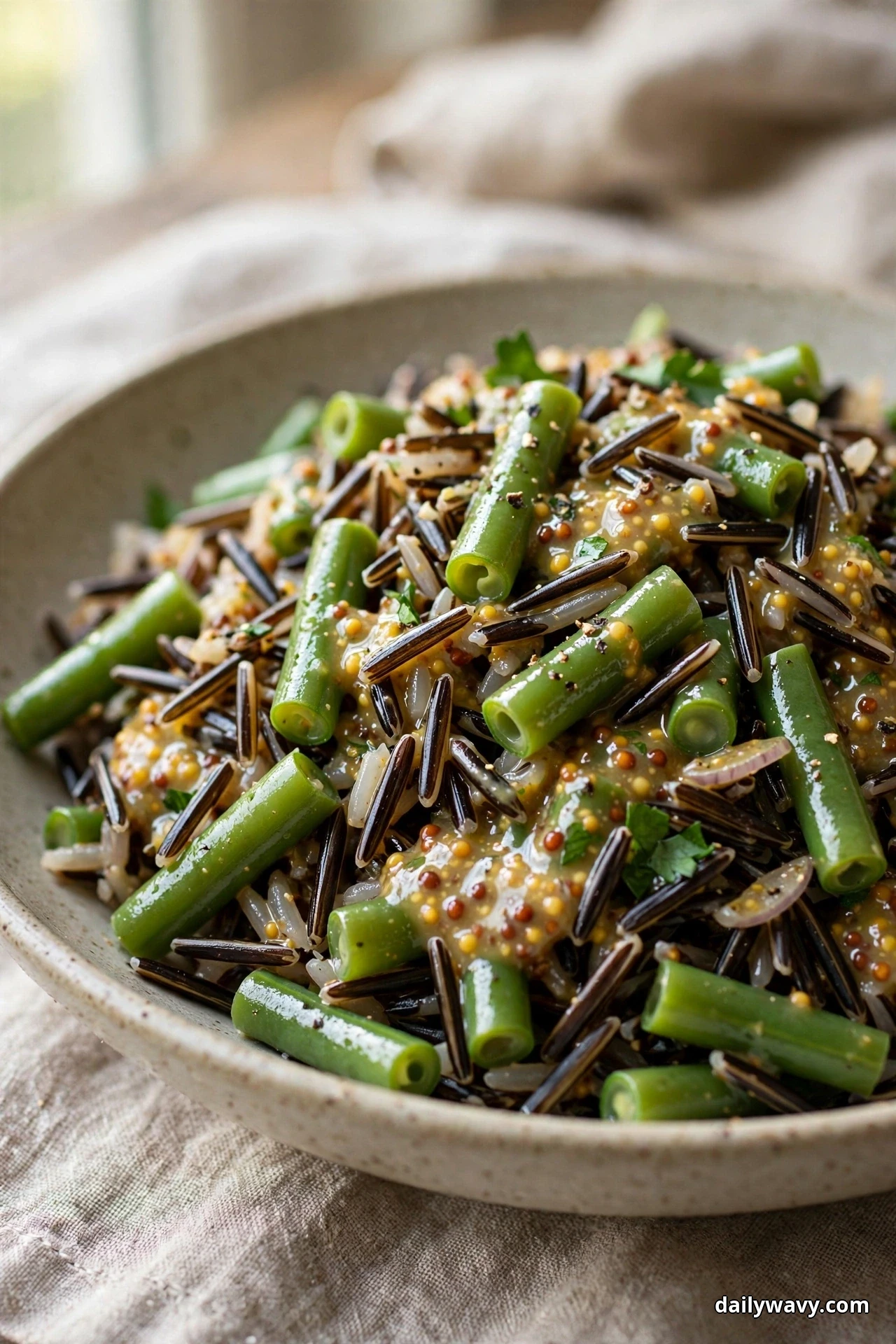 A close view of wild rice salad with bright green bean pieces coated in a whole-grain mustard dressing fills a speckled bowl