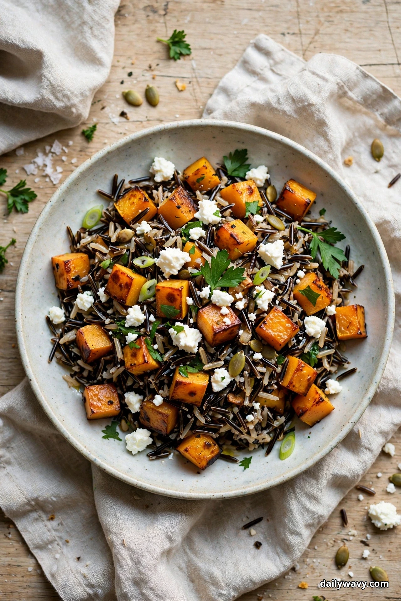 An overhead view shows a bowl of wild rice salad with caramelized roasted butternut squash cubes, crumbled feta and pumpkin seeds