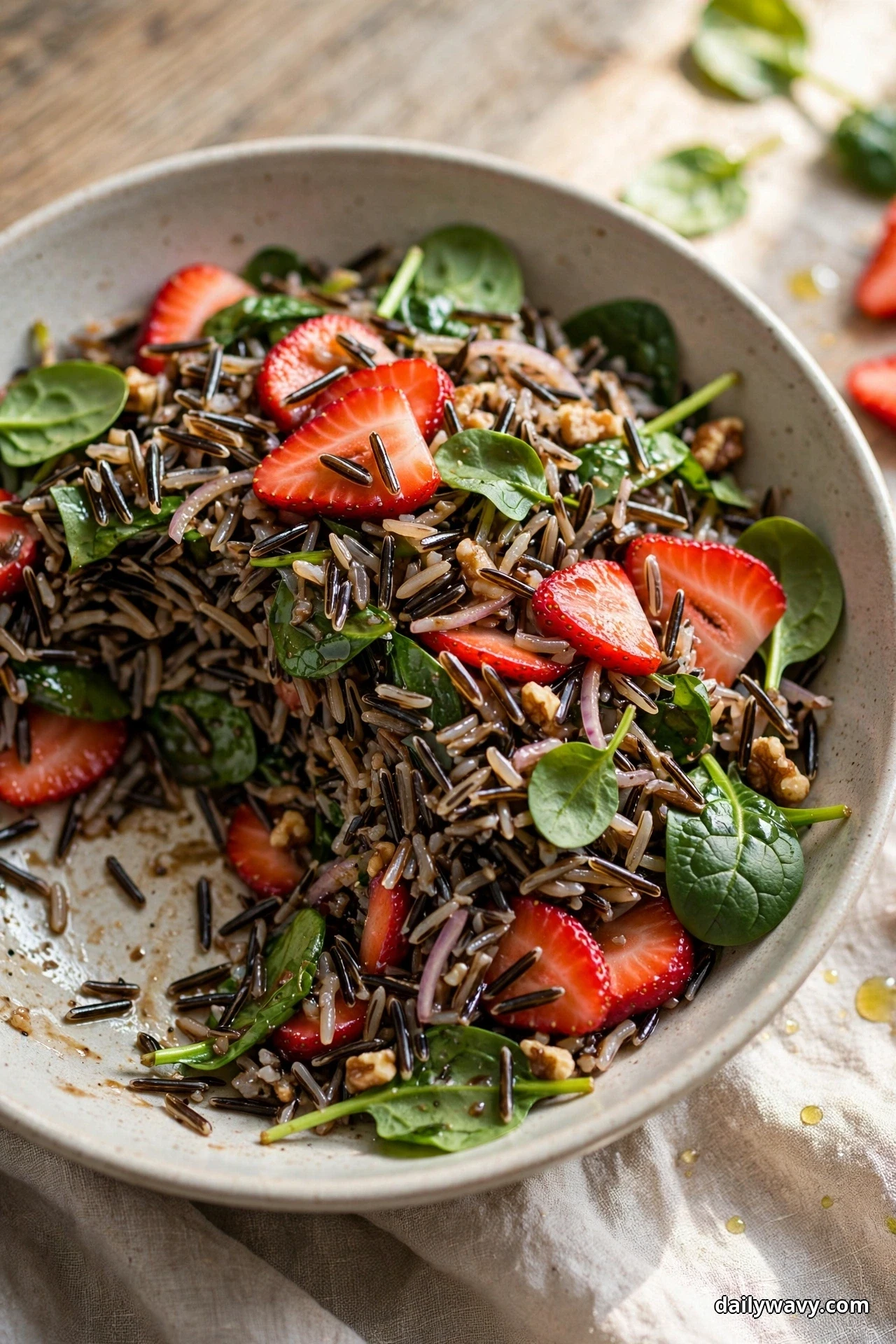 A bowl of wild rice salad with baby spinach leaves and sliced strawberries has one serving removed