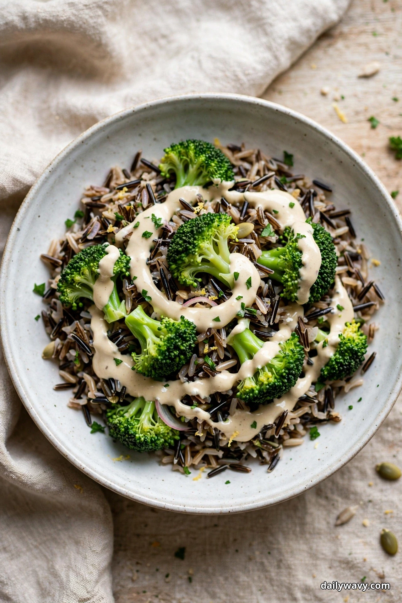 An overhead view shows a bowl of wild rice salad with bright broccoli florets under a creamy tahini drizzle