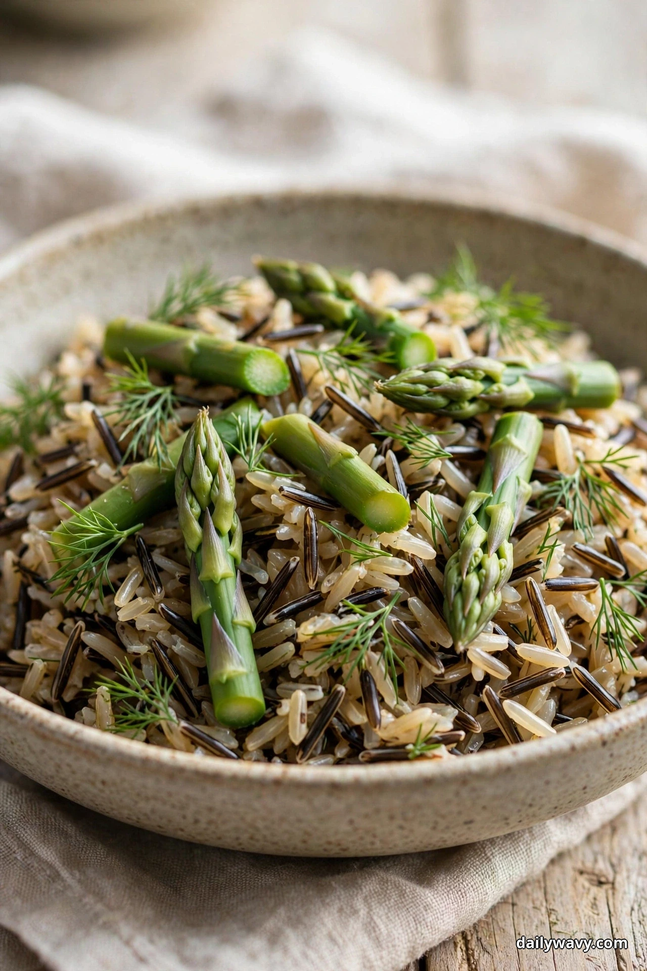 A close view of wild rice salad topped with blanched asparagus pieces and fresh dill fronds fills a speckled bowl
