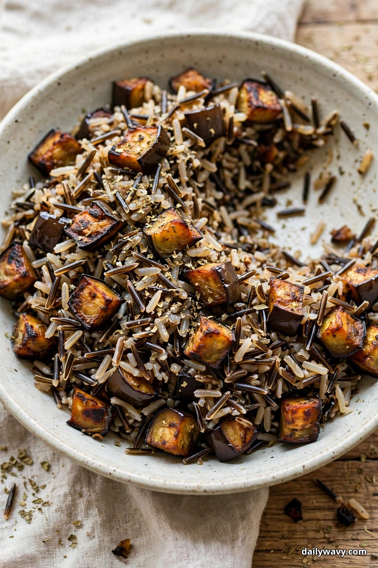 A bowl of wild rice salad with caramelized roasted eggplant cubes and dried oregano has one serving removed